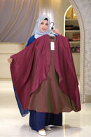 Woman holding a batwing shrug of modest collection in front of a mirror