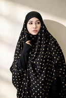 Woman wearing a black hijab with gold polka dots against a neutral background