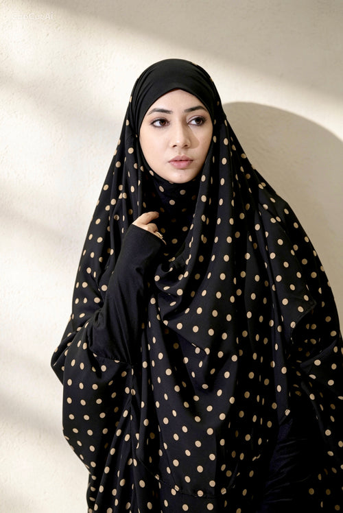 Woman wearing a black hijab with gold polka dots against a neutral background