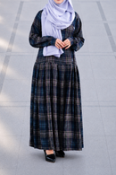 A woman wearing a long-sleeved navy and black plaid maxi dress with a matching navy hijab, standing on a gray tiled outdoor walkway.