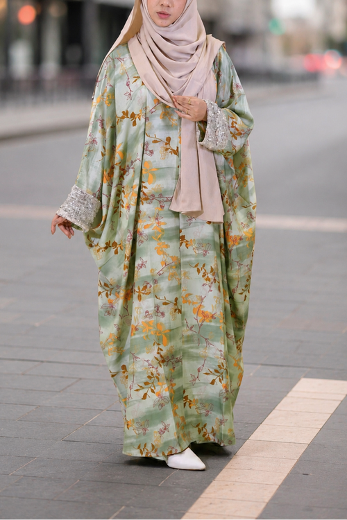Woman in a floral kaftan dress and hijab walking on a city street.