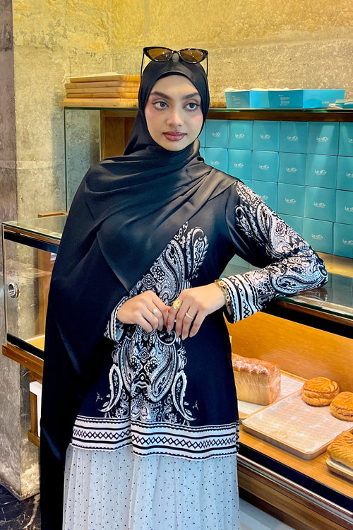 Woman in a black and white dress standing in front of a bakery display case.