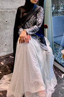 A woman sitting down wearing a voluminous milky white tulle skirt with black polka dots, showing the layered fabric and nylon lining
