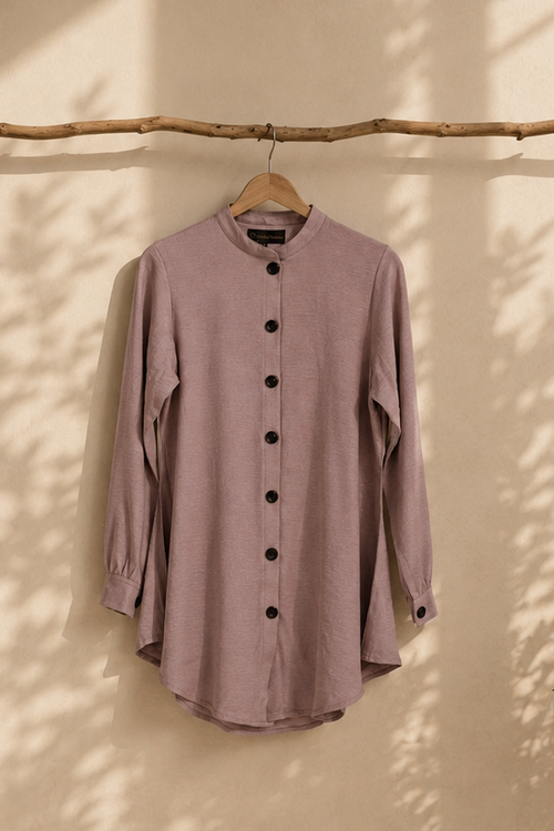 Dusty pink ladies summer modest shirt hanging against a warm beige Mediterranean-style wall with soft natural daylight, olive branch shadows, and minimalist editorial aesthetic.
