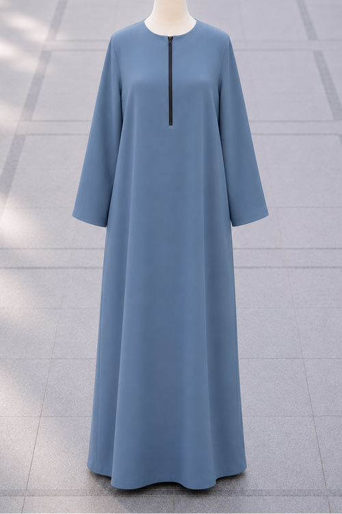 A light blue long abaya dress displayed on a mannequin torso, featuring a straight silhouette, long sleeves, and a small black zipper detail at the neckline, set against a gray tiled floor.