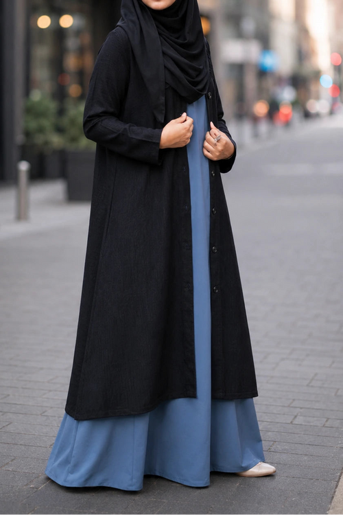 Woman wearing a black hijab and a long black and blue dress on a city street.