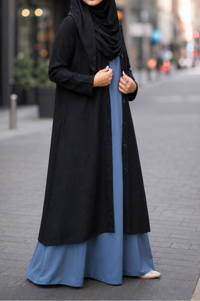Woman wearing a black hijab and a long black and blue dress on a city street.