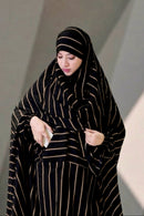Front view of a woman wearing the black and gold striped Urban Stripe Khimar, demonstrating the functional side pocket.