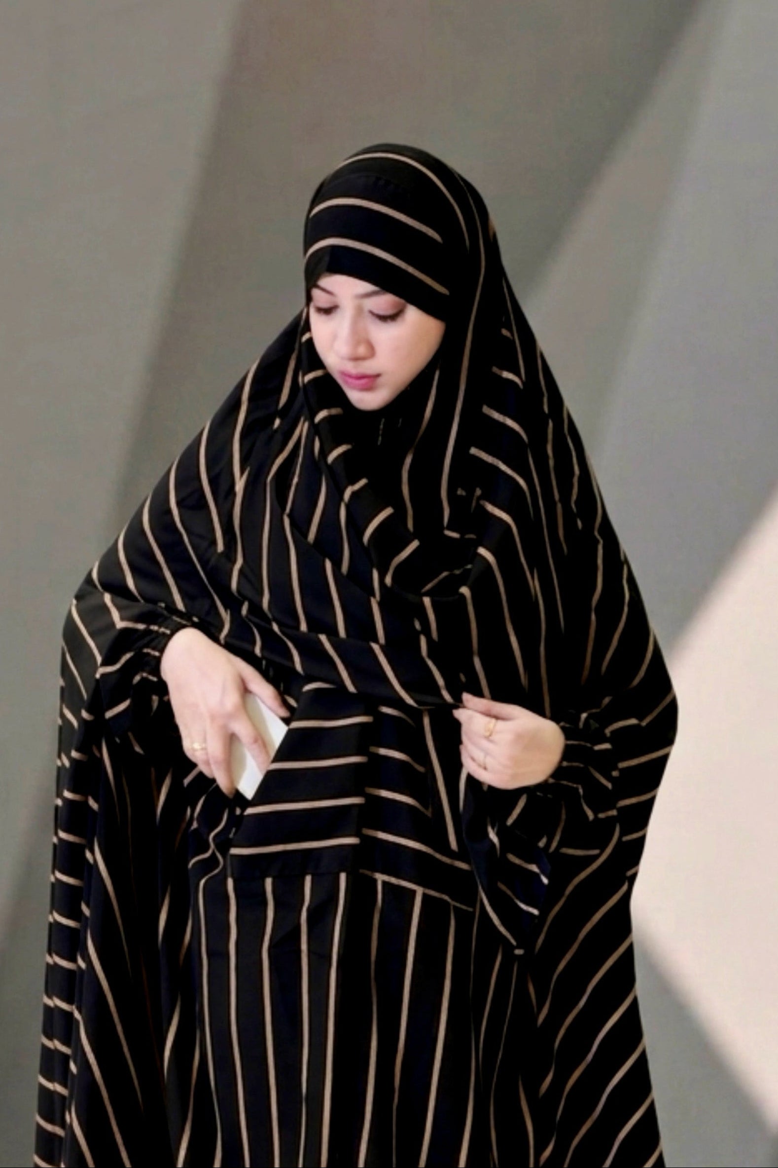 Front view of a woman wearing the black and gold striped Urban Stripe Khimar, demonstrating the functional side pocket.